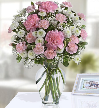 12 Pink carnations, 2 stems of white chrysanthemums and fresh greens in a Glass vase (one sided round arrangement) Reflection