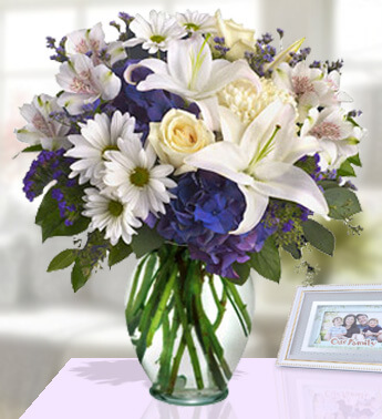 2 stems of Alstroemeria ,2 stems of White Chrysanthemums , 3 stems of White Roses ,2 stems of White Lilies, 3 stems of Purple Statice , Blue Hydrangea in clear vase. (one sided round arrangement) Ritzy Arrangement
