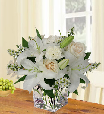 Arrangement of 2 stems of White Lilies, 4 stems of Peach Roses and 4 stems of White Carnations with fillers in a cube vase. Precious Memories
