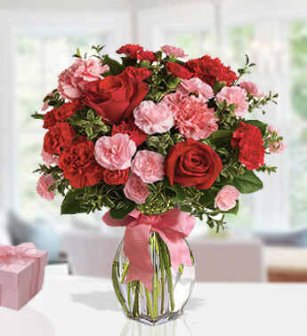 3 stems of Red Rose, 15 stems of Pink Carnation and 15 stems of Red Carnations with fillers in a glass vase. (One side round arrangement) Shades Of Red & Pink