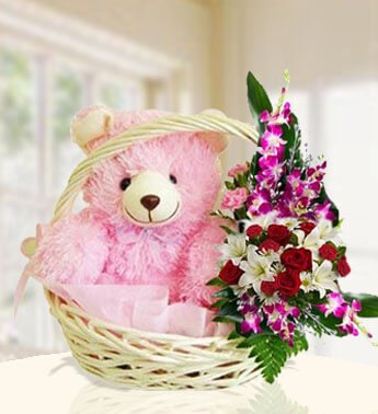 12 Inch Pink Teddy bear along an arrangement of 10 Sonia Orchids , 8 Red Roses , 2 stems of white Lilies in a basket Cuddlng Teddy
