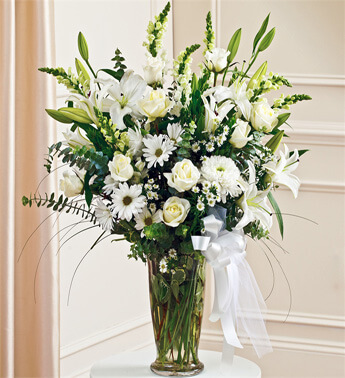 7 stems of White Lilies, 4 stems of White Chrysanthemums, 10 White Rose, 5 White Carnation with greens in a glass vase.(one sided arrangement) Perfect Tribute